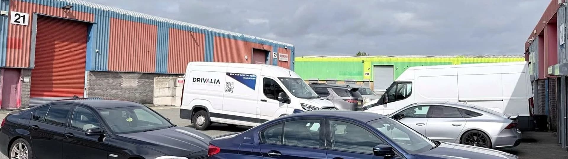 A wide view across the industrial estate yard with a Drivalia van and several fleet cars parked outside the units.